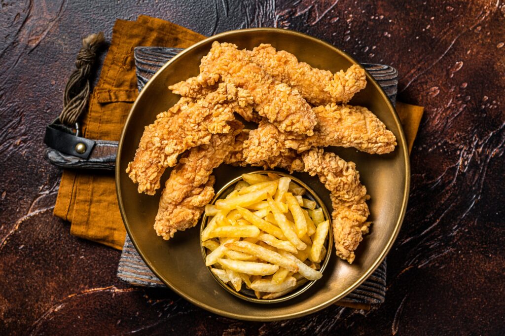 Dip fried Chicken breast strips with French Fries and sauces. Dark background. Top view